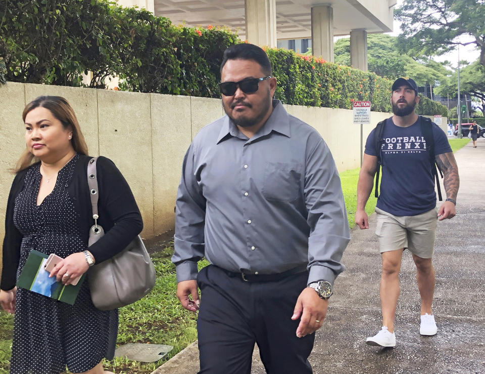 FILE - In this Sept. 25, 2019 file photo, former Honolulu police officer Reginald Ramones, center, walks down a street in Honolulu. Samuel Ingall, a homeless man, is suing the Honolulu Police Department and the city after he says officers forced him to lick a urinal in a public restroom. A U.S. judge sentenced a former Honolulu police officer Wednesday, July 15, 2020, to four years in prison, telling him to imagine someone doing that to his two young daughters. The homeless man was just as defenseless and powerless as John Rabago's 10- and 8-year-old daughters, U.S. District Judge Leslie Kobayashi said. (AP Photo/Jennifer Sinco Kelleher, File)