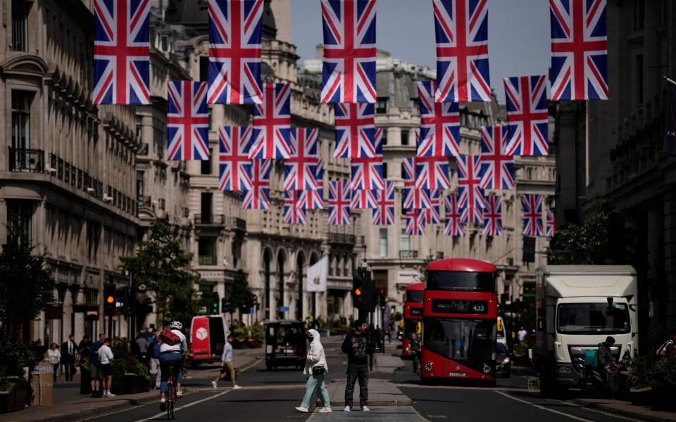  People cross the Regent Street shopping district with Union flags hanging over it to mark the upcoming Platinum Jubilee - Matt Dunham/ AP