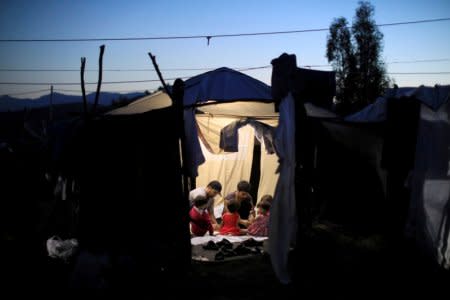 Two migrant men and four babies sit inside a tent at a makeshift camp next to the Moria camp for refugees and migrants on the island of Lesbos, Greece, September 18, 2018. REUTERS/Giorgos Moutafis