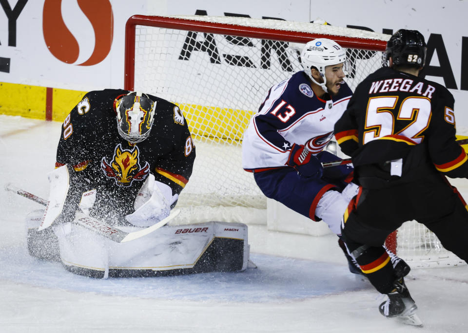 Columbus Blue Jackets forward Johnny Gaudreau, center, is checked by Calgary Flames defenseman MacKenzie Weegar, right, as Flames' goalie Dan Vladar hangs onto the puck during first-period NHL hockey game action in Calgary, Alberta, Monday, Jan. 23, 2023. (Jeff McIntosh/The Canadian Press via AP)