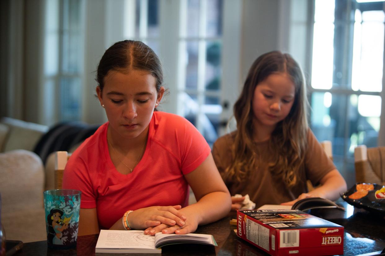 Myleigh Eason, 11, at front, and her sister Madelyn, 9, read and snack together in their kitchen after coming home from school in Spring Hill, Tenn., Monday, April 15, 2024.