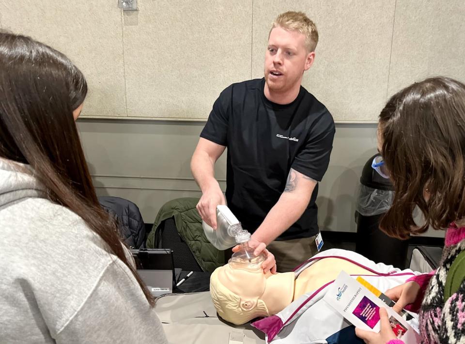 Simulation specialist Ryan Power demonstrates a resuscitation technique for a couple of high school students.