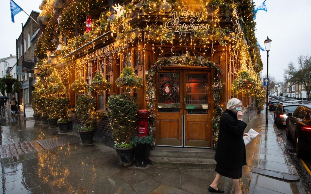 A woman in a face mask walks on deserted streets past the closed Churchill Arms pub in Kensington, west London -  Dominic Lipinski/PA