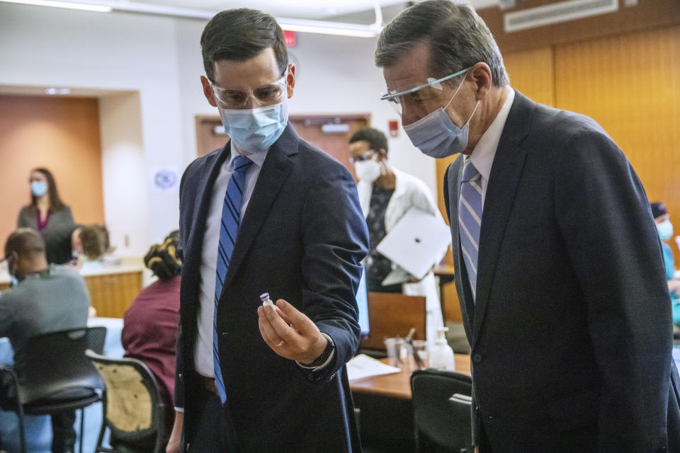 FILE - In this Dec. 17, 2020, file photo, Dr. Dan Schenkat shows Gov. Roy Cooper, right, a vial containing COVID-19 vaccine at UNC Health in Chapel Hill, N.C., where frontline healthcare workers are among some of the first recipients of the Pfizer COVID-19 vaccine. With frustration rising over the slow rollout of the vaccine, state leaders and other politicians are turning up the pressure, improvising and seeking to bend the rules to get shots in arms more quickly. (Travis Long/The News & Observer via AP, File)