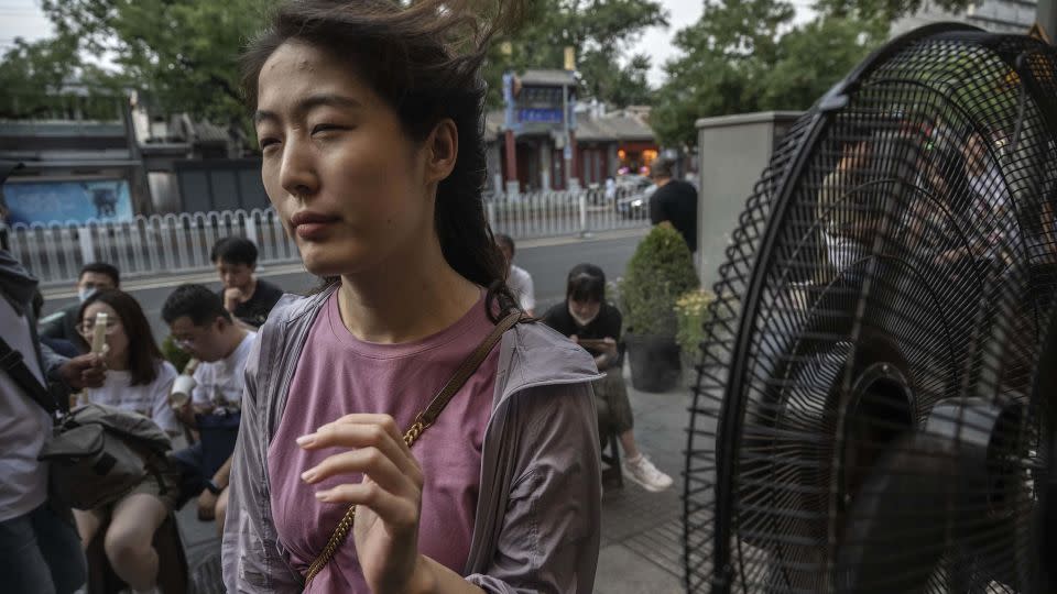 A woman cools herself on a misting fan as she waits for a table outside a popular local restaurant during a heatwave on June 23, 2023 in Beijing, China.  - Kevin Frayer/Getty Images