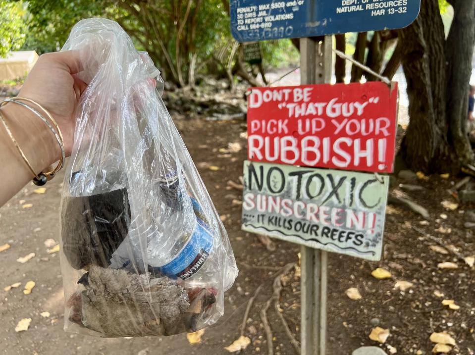 writer holding a bag of garbage in front of a no rubbish sign