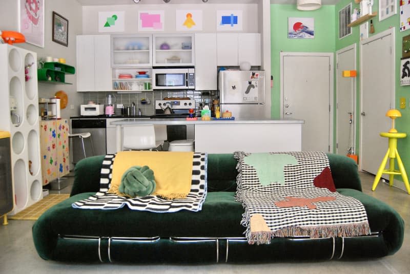 Green velvet sofa in living area across from  apartment kitchen.