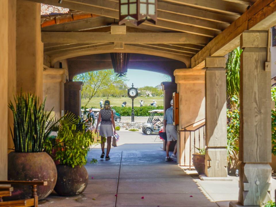 A wooden arch way with people walking towards a golf course and a black watch tower