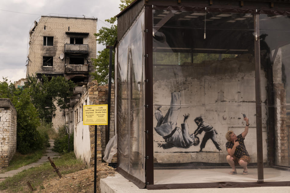 A woman takes a selfie with Banksy's artwork on the wall of a building damaged by Russian attacks in Borodyanka, Ukraine, Wednesday, Aug. 2, 2023. Borodyanka was occupied by Russian troops at the beginning of their full-scale invasion last year. (AP Photo/Jae C. Hong)