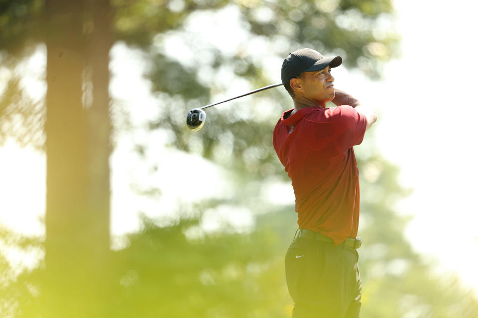 Tiger Woods swings and watches his ball travel.