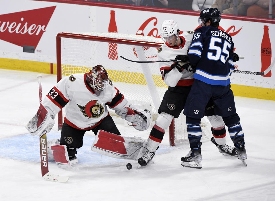 Ottawa Senators goaltender Cam Talbot (33) looks to cover the puck as Winnipeg Jets' Mark Scheifele (55) is checked by Senators' Shane Pinto (57) during the second period of an NHL hockey game Tuesday, Dec. 20, 2022, in Winnipeg, Manitoba. (Fred Greenslade/The Canadian Press via AP)