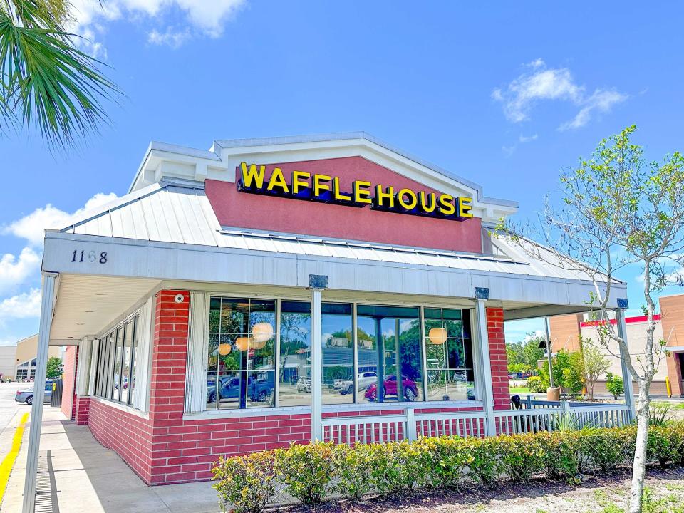 Waffle House building, which is red with a white roof and porch area. The lettering on the building is yellow.