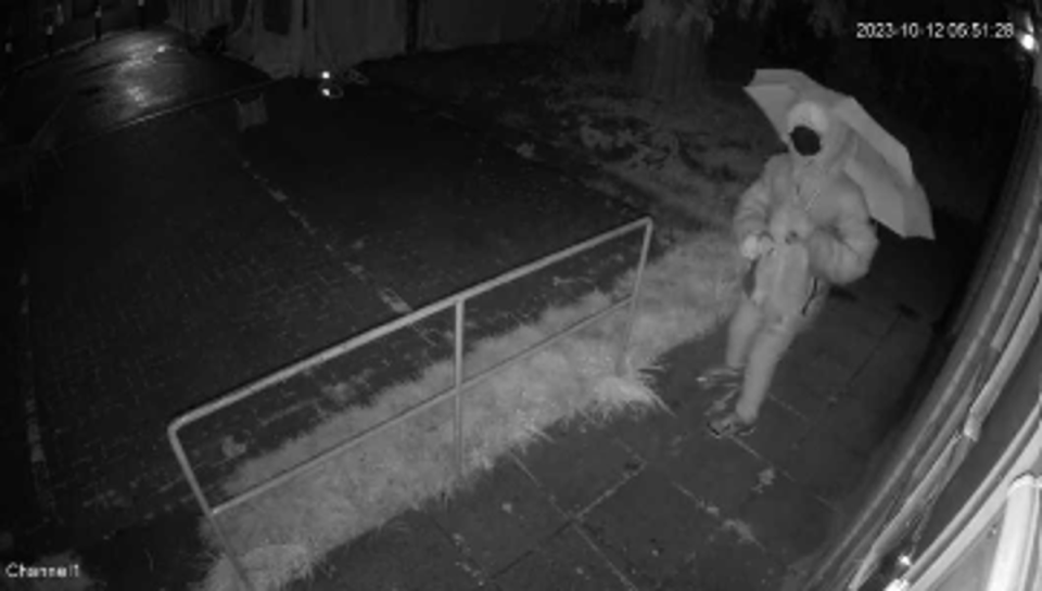 CCTV shows a figure in a mask and carrying an umbrella before throwing the red paint (Twitter)