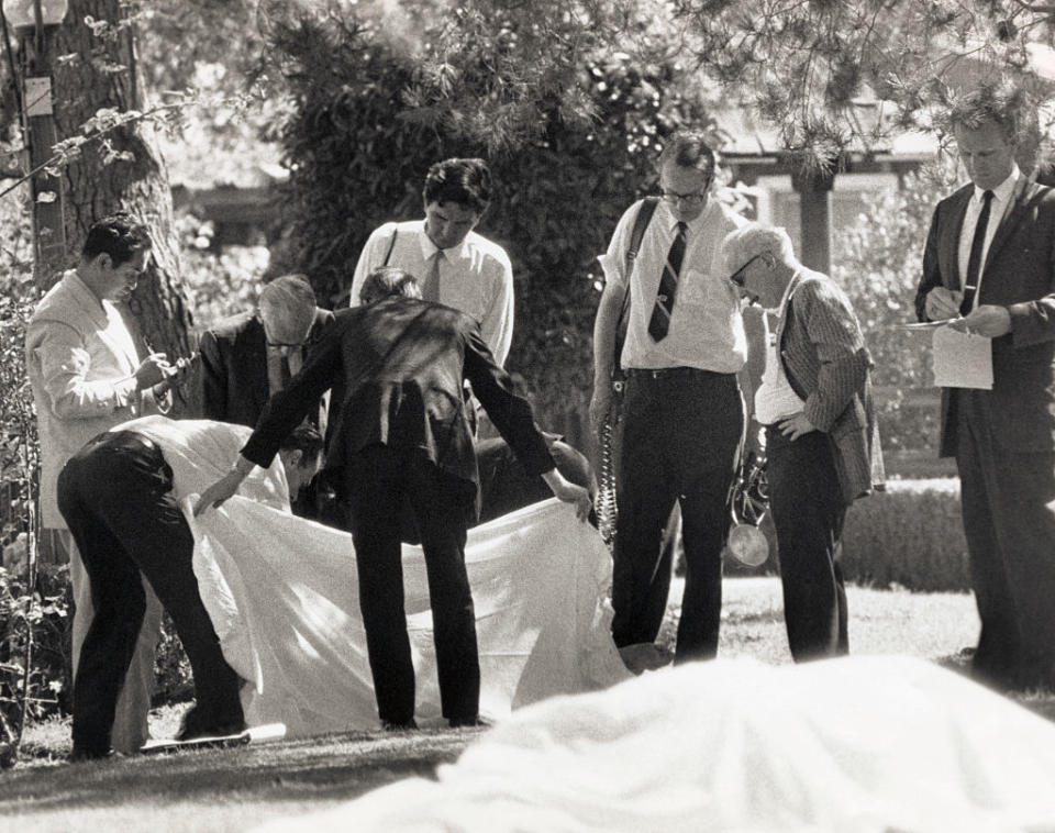 County Coroner Thomas Nogouchi (left) takes notes as assistants hold a sheet which covered one body as the other of the two bodies found on the lawn of the Sharon Tate-Roman Polanski home. (Credit: Getty Images)