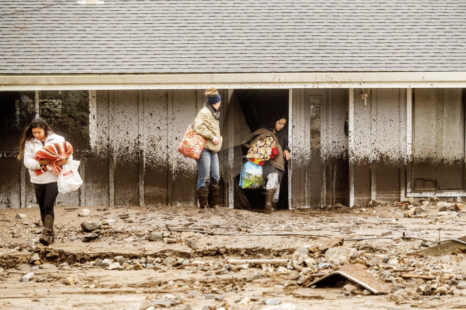 Hana Mohsin, right, carries belongings from a neighbor's home which was damaged in a mudslide on Wednesday, Jan. 27, 2021, in Salinas, Calif. The area, located beneath the River Fire burn scar, is susceptible to landslides as heavy rains hit hillsides scorched during last year's wildfires. (AP Photo/Noah Berger)