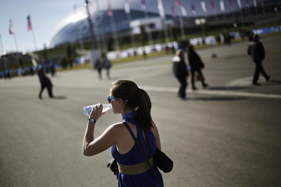 In this Wednesday, Feb. 12, 2014, photo, Kaylee Weil, of San Diego, Calif., takes a drink of water while walking through the Olympic Park wearing a sun dress at the 2014 Winter Olympics, in Sochi, Russia. Temperatures were near 60 degrees Fahrenheit in Sochi on Wednesday. (AP Photo/David Goldman)