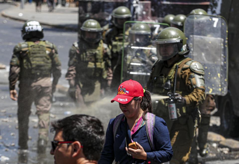 A Chilean police officer sprays pepper gas at a female anti-government demonstrator near to La Moneda presidential palace in Santiago, Chile, Tuesday, Nov. 12, 2019. Chile celebrates on Tuesday 26 days of mobilizations with a large demonstration in Santiago and a general strike of the general activity that froze the activity in the coastal city of Valparaíso and other parts of the country in demand of social improvements, while the dollar reached historical values and Begins to be cause for concern. (AP Photo/Esteban Felix)