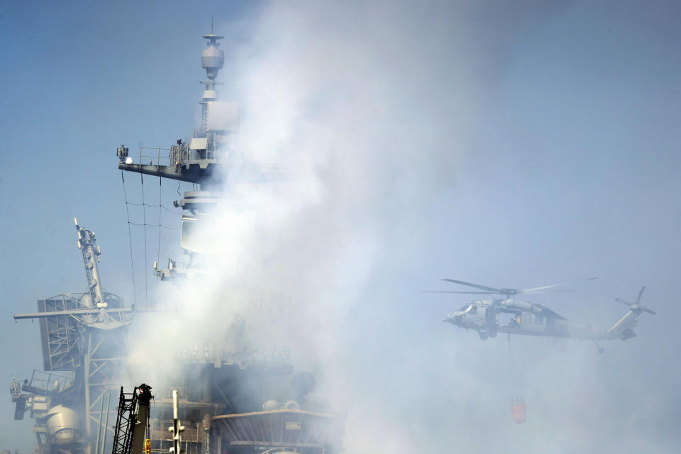 A helicopter approaches the USS Bonhomme Richard as crews fight the fire, Monday, July 13, 2020, in San Diego. Fire crews continue to battle the blaze Monday after numerous people suffered minor injuries in an explosion and fire Sunday on board the USS Bonhomme Richard at Naval Base San Diego. (AP Photo/Gregory Bull)