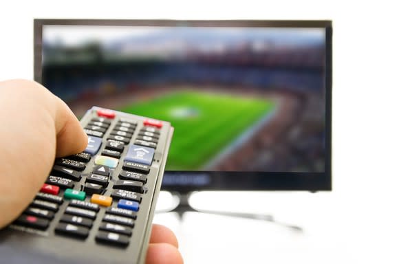 A person holding a TV remote pointed at a TV in the background.