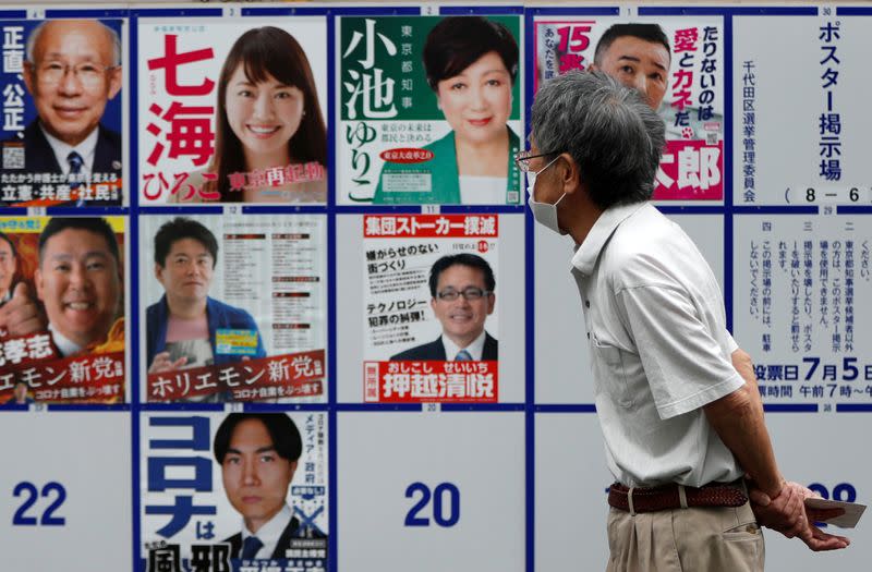 A voter watches candidate posters, including current governor Yuriko Koike, for the Tokyo Governor election in front of a voting station amid the coronavirus disease (COVID-19) outbreak, in Tokyo