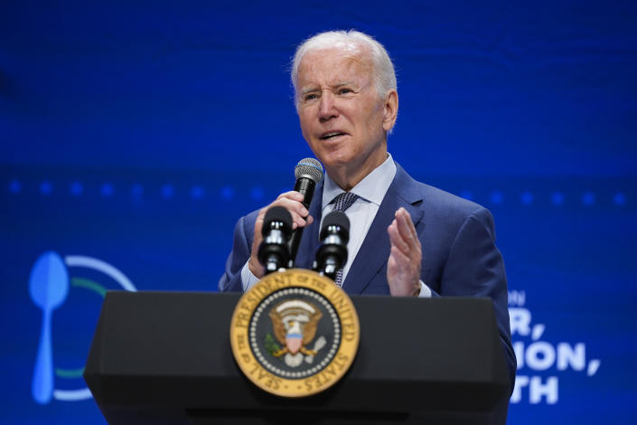 El presidente Biden se para en un podio con el sello presidencial mientras se acerca un micrófono a la boca.