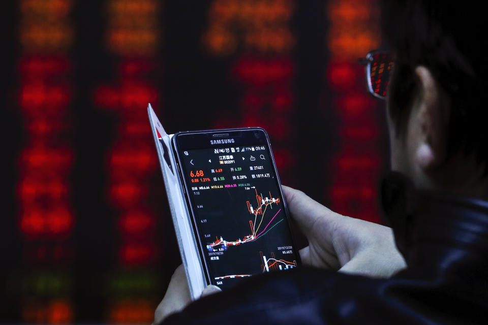 An investor checks stock prices through his smartphone at a brokerage house in Beijing, Friday, Dec. 20, 2019. Stocks were mixed in early trading in Asia on Friday after Wall Street posted more record highs, extending the market's gains for the week. (AP Photo/Andy Wong)