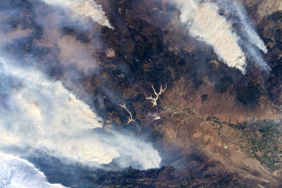 wildfire smoke plumes rise from california mountains surrounding a valley as seen from space