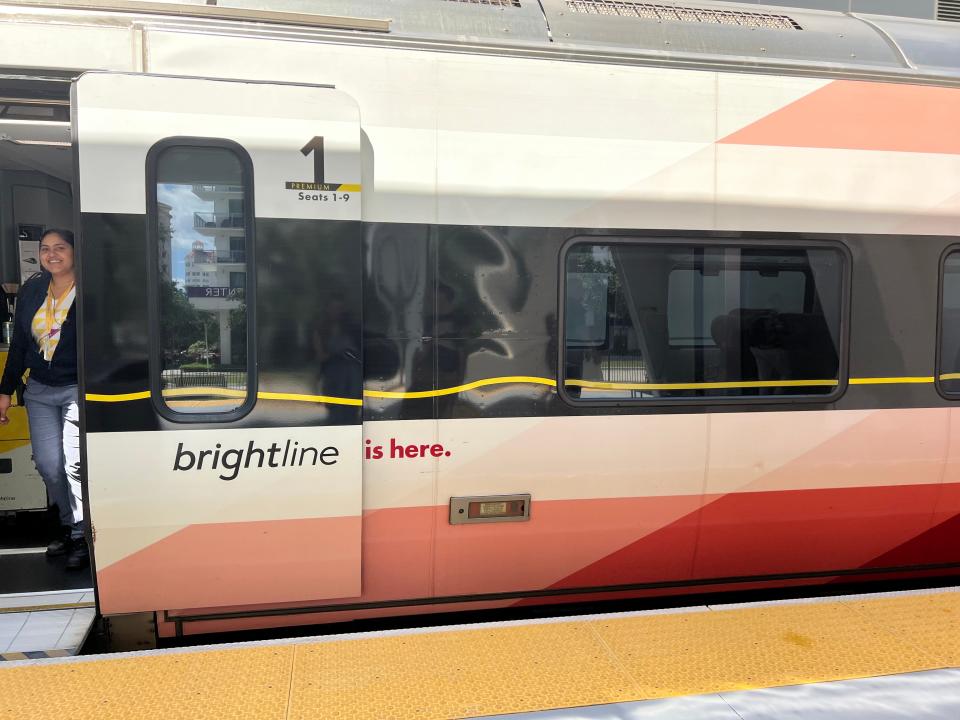 The outside of a Brightline train is shown, a server peeks out of an open door.