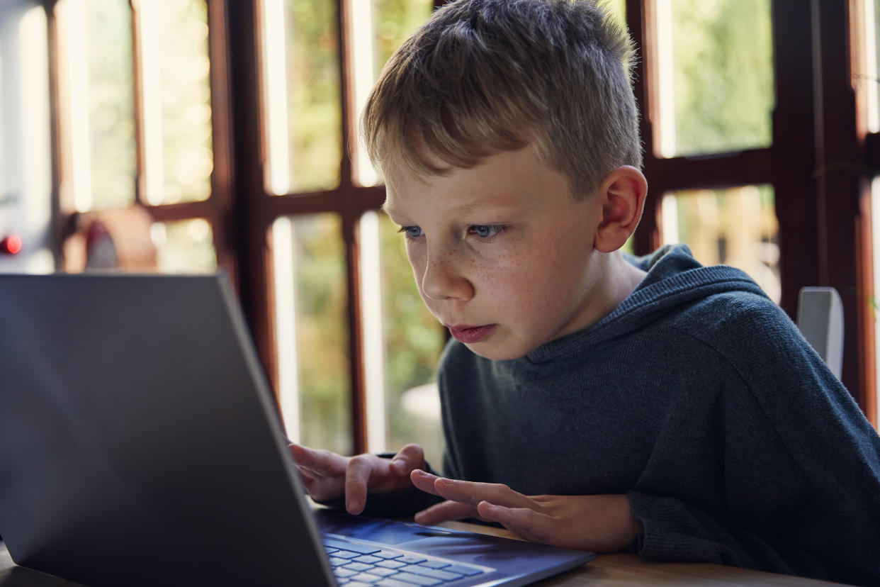 Young boy doing school work at home, working on a laptop