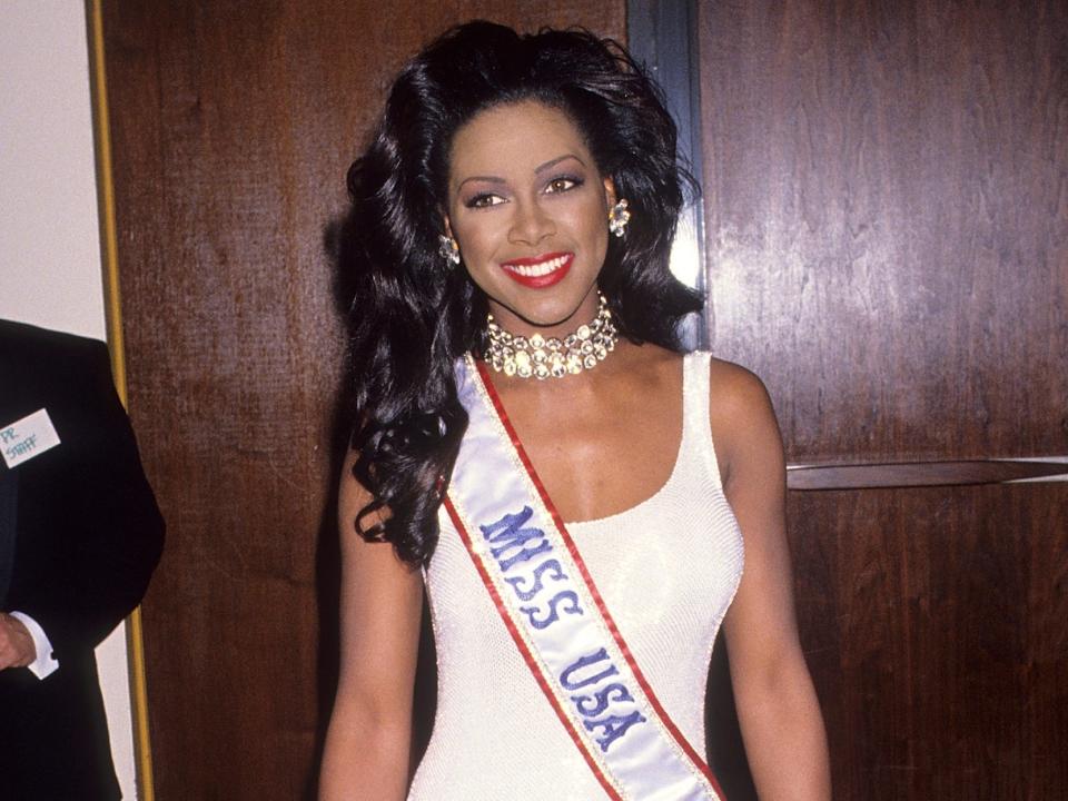 Miss USA Kenya Moore stands in a white dress and her sash in 1993.