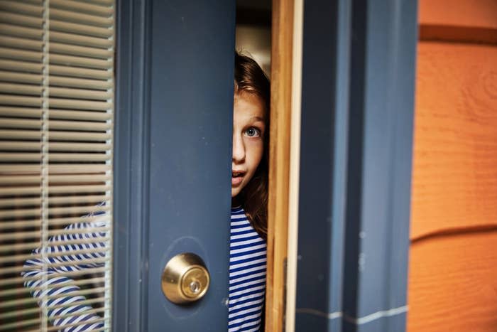 Young child peeking through partially open door, wearing a striped shirt