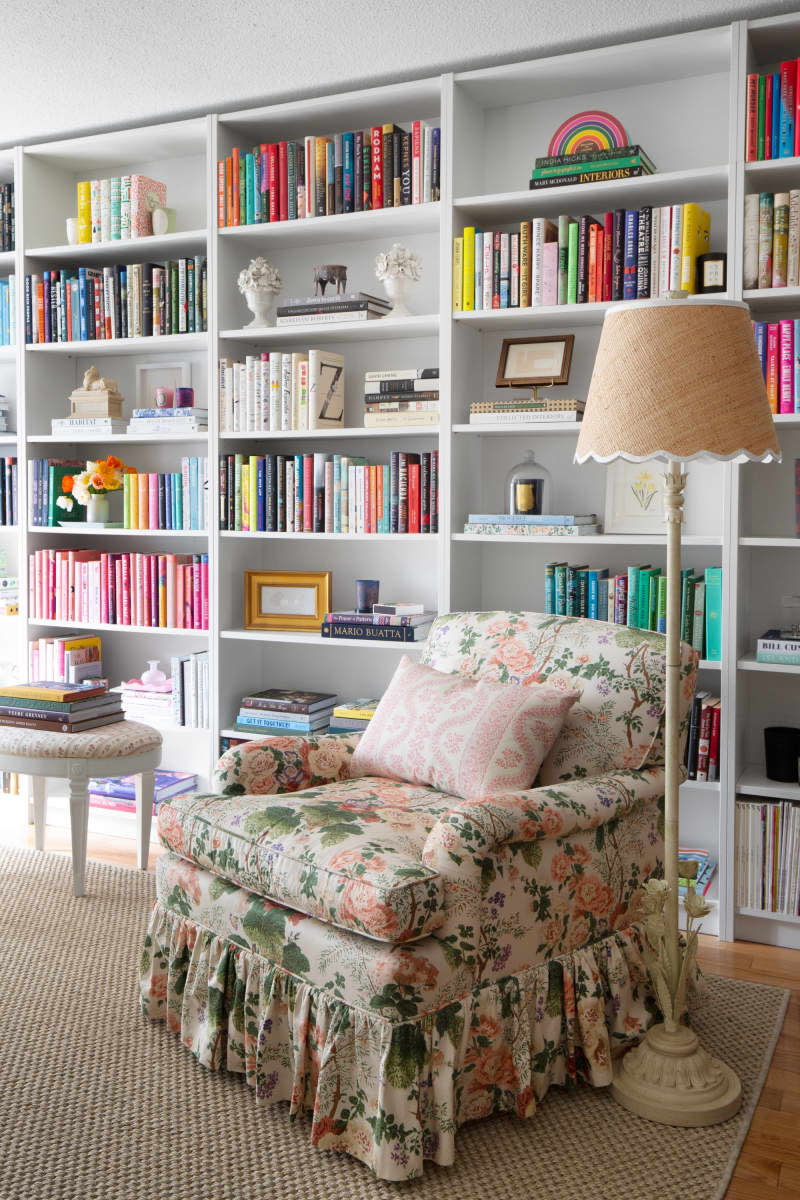 floor to ceiling color coded book shelf wall, floral chair with skirt