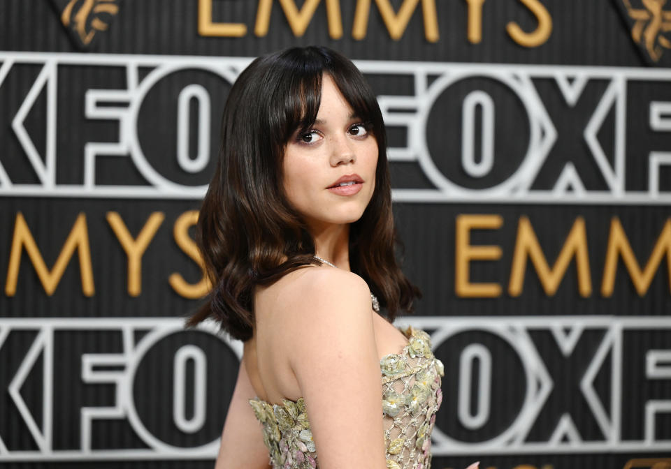 Jenna Ortega poses on the red carpet at the Emmys, wearing a strapless floral-patterned gown