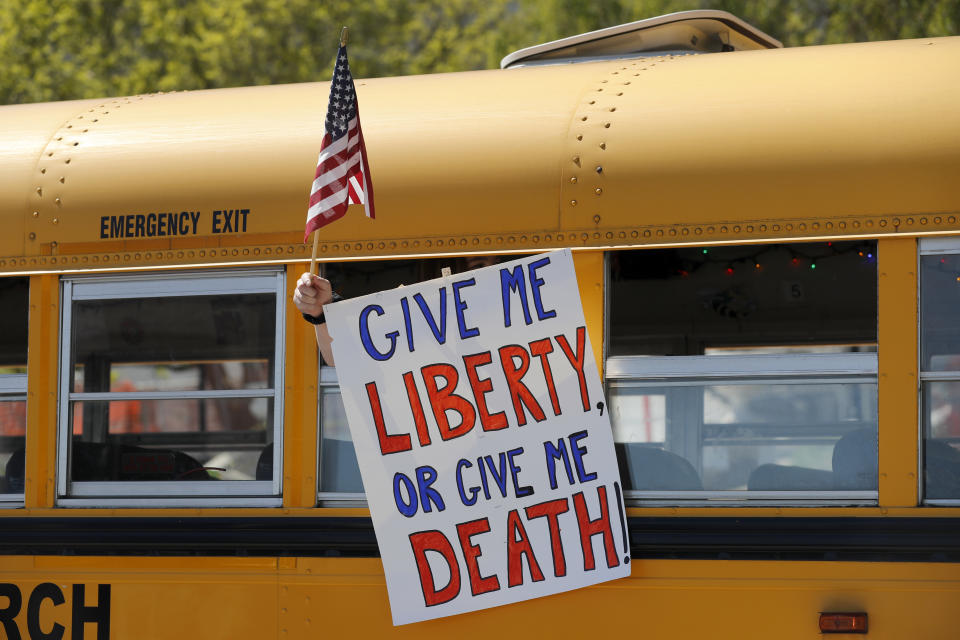 A person holds a sign while waving a flag in the direction of people gathered voice their opposition to stay-at-home orders put into place due to the COVID-19 outbreak outside the Missouri Capitol Tuesday, April 21, 2020, in Jefferson City, Mo. Several hundred people gathered to protest the restrictions and urge a restart to the economy shutdown due to the coronavirus. (AP Photo/Jeff Roberson)