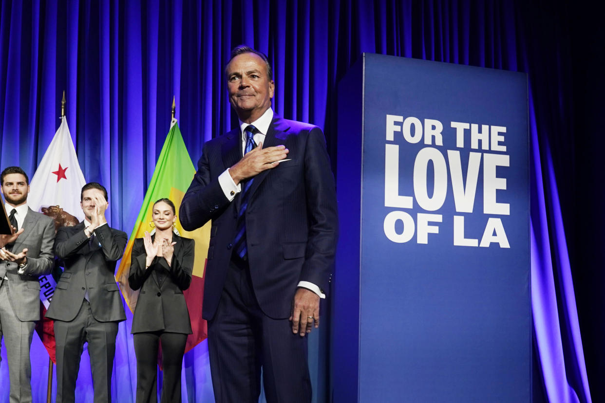 Los Angeles mayoral candidate Rick Caruso walks across a stage. A sign behind him reads: For the love of L.A.