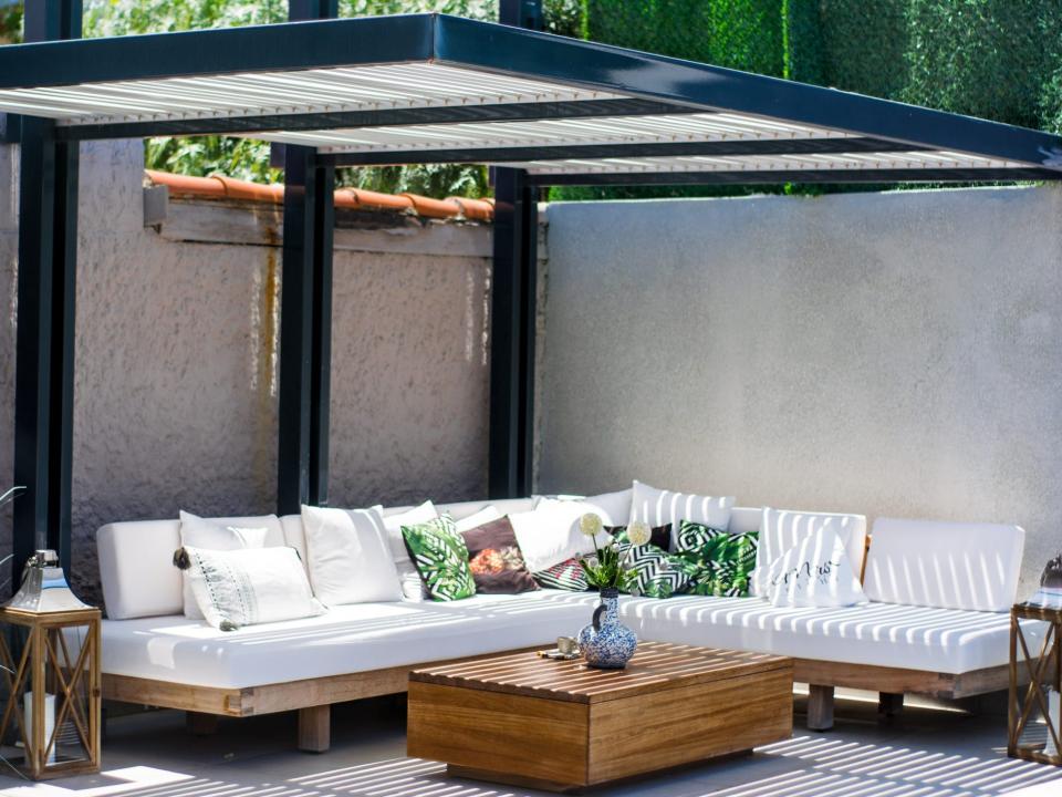 An L-shaped couch with white cushions and pillows and a wooden coffee table in front of it. A black and white roof stands over the couch