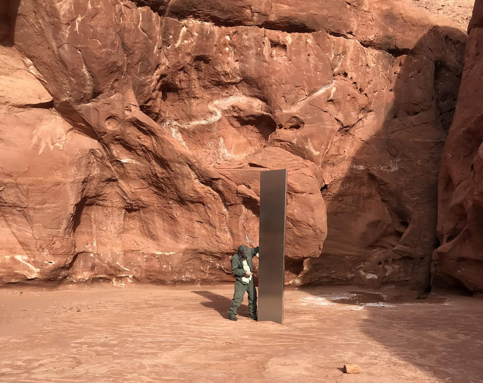 FILE - In this Nov. 18, 2020, file photo provided by the Utah Department of Public Safety, a Utah state worker stands next to a metal monolith in the ground in a remote area of red rock in Utah. The mysterious silver monolith that was placed in the Utah desert has disappeared less than 10 days after it was spotted by wildlife biologists performing a helicopter survey of bighorn sheep, federal officials and witnesses said. The Bureau of Land Management said it had received credible reports that the three-sided stainless steel structure was removed on Nov. 27. (Utah Department of Public Safety via AP, File)