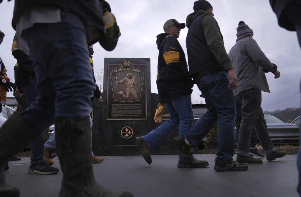 Pittsburgh Steelers fans walk past a marker commemorating the exact spot where the 1972 "Immaculate Reception," was made by Franco Harris at Three Rivers Stadium, which once stood on the North Side of Pittsburgh, on Sunday, Dec. 11, 2022, in Pittsburgh, Pa. Harris' scoop of a deflected pass and subsequent run for the winning touchdown in a 1972 playoff victory against Oakland has been voted the greatest play in NFL history and celebrates its 50th anniversary this year. (AP Photo/Jessie Wardarski)