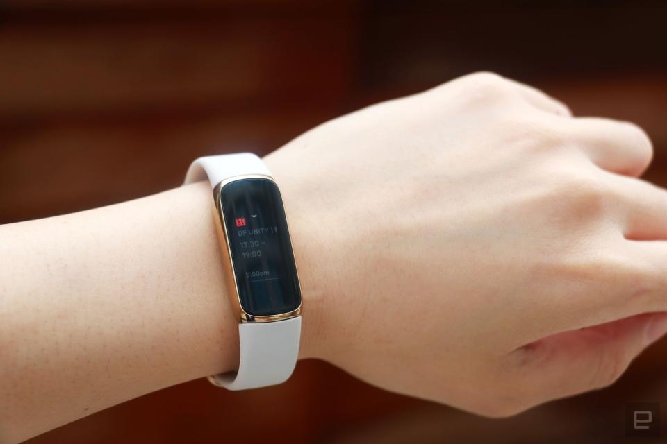 <p>Slightly off angle view of the Fitbit Luxe with a light pink silicone band on a wrist against a dark brown background. The screen shows a calendar notification for an event from 5:30pm to 7pm.</p>
