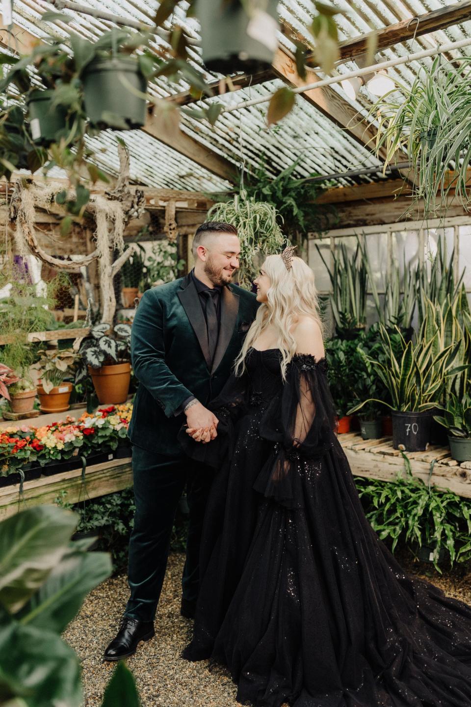 A bride and groom look at each other in a greenhouse wearing their wedding attire.