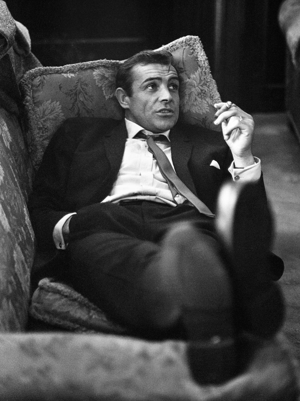 <p>Connery lounges on a sofa with a cigarette during the filming of ‘Woman of Straw’ in 1963</p>Getty