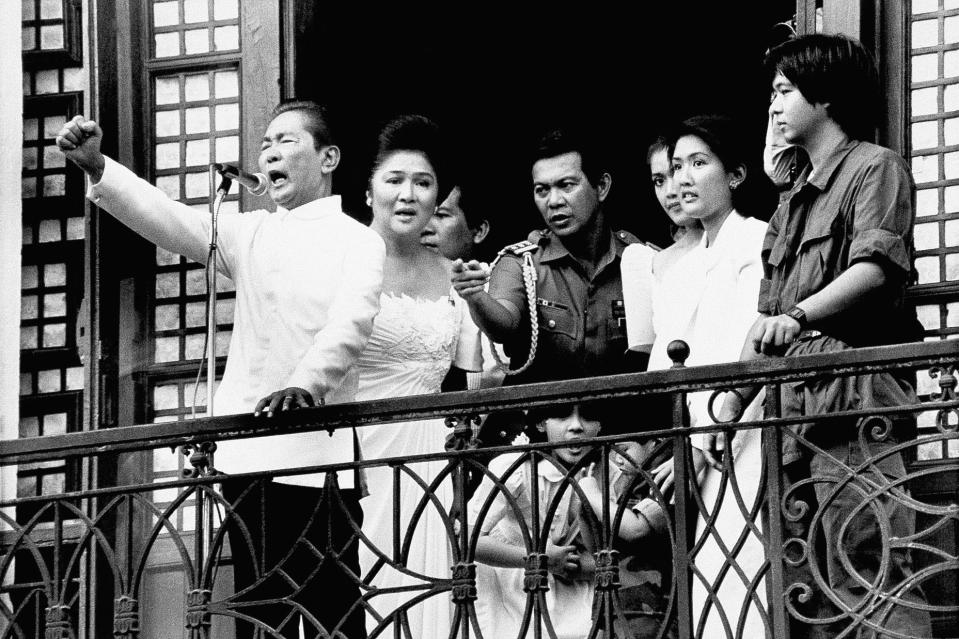 Ferdinand Marcos with his wife Imelda at his side gestures from the balcony of Malacanang Palace, Feb. 25, 1986, in Manila, just after taking the oath of office as President of the Philippines. Just hours later, Marcos resigned and fled to the U.S. Air Force's Clark Air Base, 50 miles northwest of Manila, as he prepared to accept an American offer to fly him out of the Philippines amid huge protests against his rule. / Credit: Alberto Marquez/AP