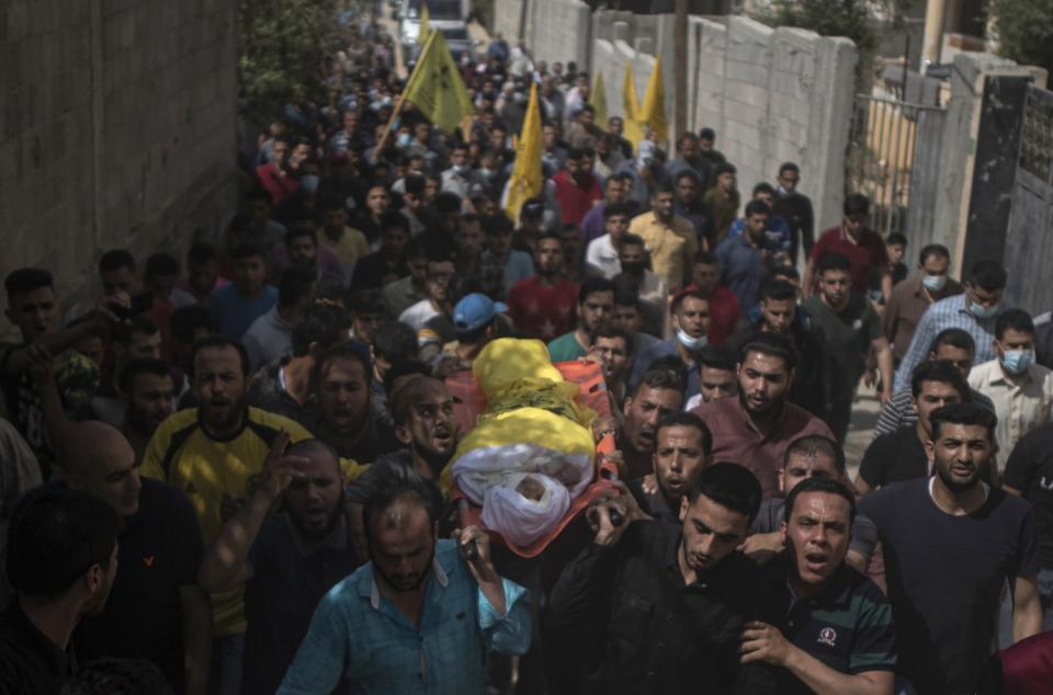 Mourners carry a body wrapped in white and yellow on a sling amid a throng of people