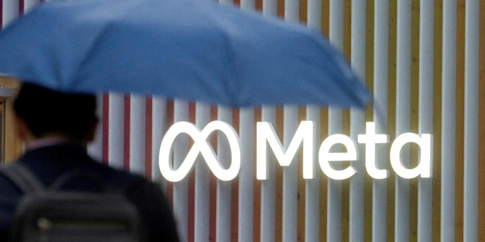 Man with blue umbrella with back against Meta logo.