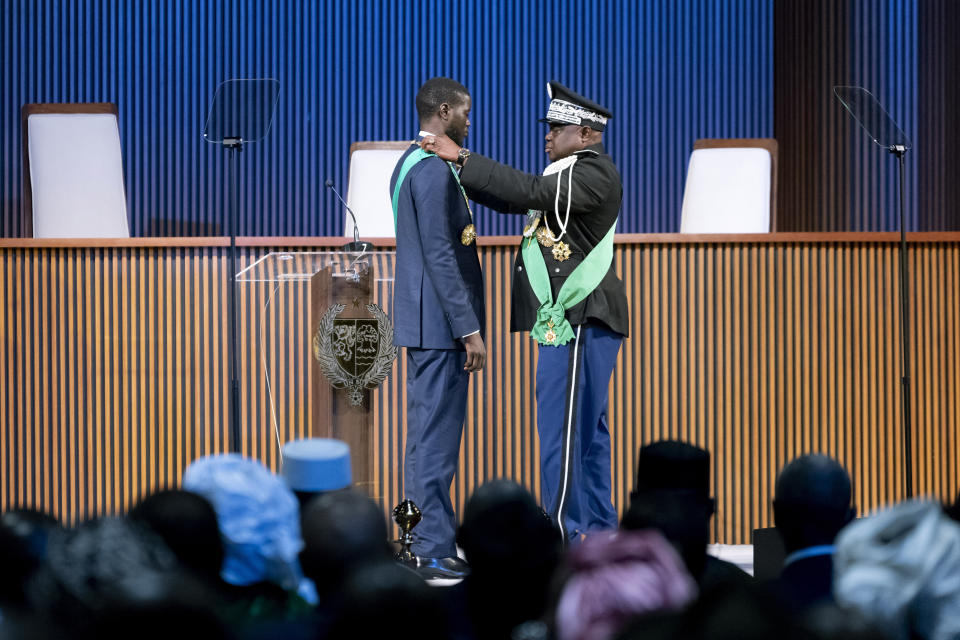 Bassirou Diomaye Faye, centre left, receives the Necklace of the Grand Master of the National Order of the Lion during his swearing in ceremony as Senegal's president in Dakar, Senegal, Tuesday, April 2, 2024. Senegal has sworn in Bassirou Diomaye Faye as its new president, completing the previously little-known opposition figure’s dramatic ascent from prison to the palace in recent weeks. Faye was released from prison less than two weeks before the March election following a political amnesty announced by the outgoing president. (AP Photo/Sylvain Cherkaoui)