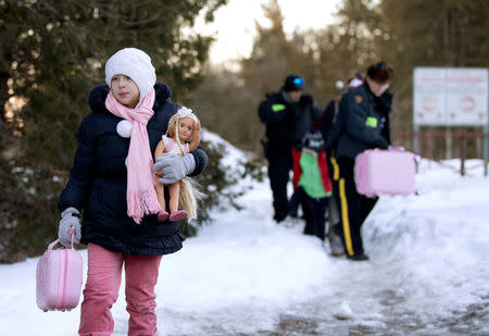 A young girl carries her doll and suitcase as her family that claimed to be from Turkey are met by Royal Canadian Mounted Police (RCMP) officers after they crossed the U.S.-Canada border illegally leading into Hemmingford, Quebec, Canada March 20, 2017. REUTERS/Christinne Muschi/File Photo