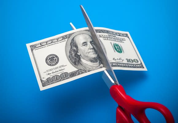 A pair of scissors cutting a $100 bill.