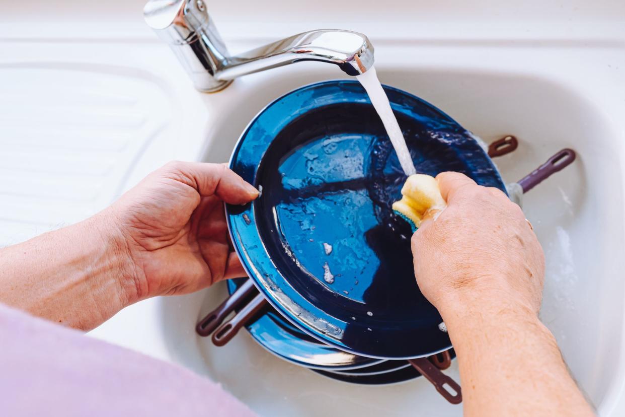 man doing homework washes large pile of dishes in kitchen sink, household chores, routine, duties