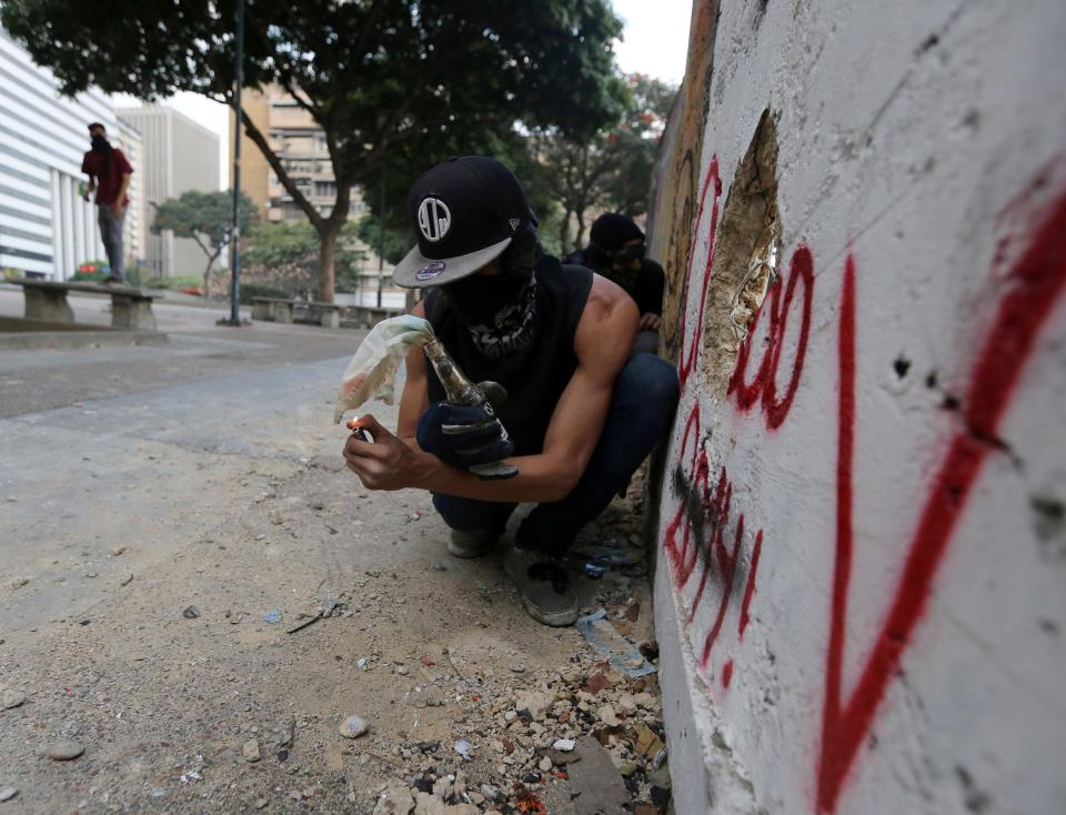 A demonstrator lights a molotov bomb as he readies to throw it against Bolivarian National Police officers during clashes in Caracas, Venezuela, Thursday, March 6, 2014. A National Guardsman and a civilian were killed Thursday in a clash between residents of a Caracas neighborhood and armed men who tried to remove a barricade, Venezuelan officials said. (AP Photo/Fernando Llano)