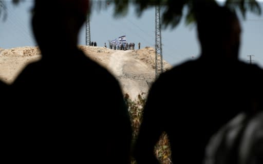 Israeli settlers wave their national flag on a hill overlooking the Palestinian Bedouin village of Khan al-Ahmar in the occupied West Bank on July 5, 2018